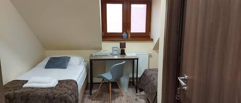 A small, single-room accommodation with two beds, a desk, and a chair.