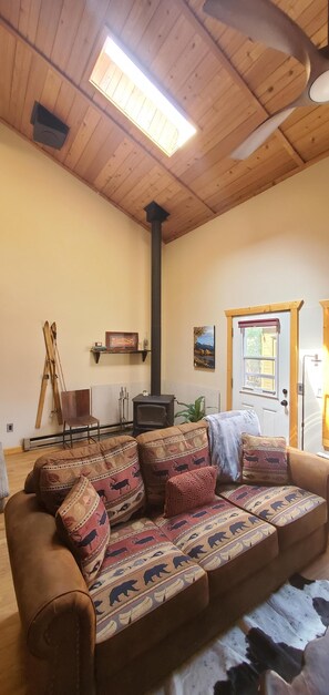 Ein gemütliches Wohnzimmer mit Holzbalkendecke, einer Couch mit gemusterten Kissen, einem Kamin und einer Tür mit Fenster.