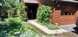 Ein Holzhaus mit Garage, ein Garten mit verschiedenen Pflanzen und ein Weg zum Eingang.