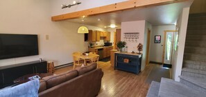 Ein Wohnzimmer mit einer Couch, einem Fernseher, einem Esstisch und einer Küchenzeile mit Holdekor und blauer Arbeitsplatte.