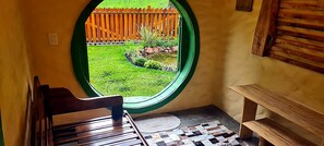 Une piĂšce dotĂ©e dâune fenĂȘtre circulaire, dâun banc en bois et dâun petit jardin visible Ă travers la fenĂȘtre.