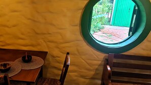 A room with a round window, a wooden table with a woven placemat, a bowl, and a chair. - CABANA TEMÁTICA DO HOBBIT - GRAMADO RURAL (Gramado)