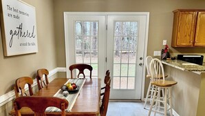 A dining room with a wooden table and chairs, a kitchen area with cabinets, and a view through the glass doors. - Rockland Creek Retreat at LKA with Water Access (Bumpass)