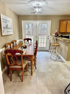 A dining room with a wooden table and chairs, a kitchen area with cabinets, and a view through the glass doors. - Rockland Creek Retreat at LKA with Water Access (Bumpass)