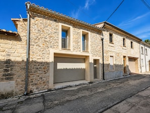 Un bâtiment en pierre avec une porte de garage, une fenêtre grillagée et un petit balcon.