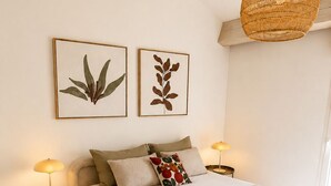 Ein Schlafzimmer mit einem Bett, zwei Nachttischen, einer Hängelampe und zwei gerahmten Pflanzenbildern an der Wand.