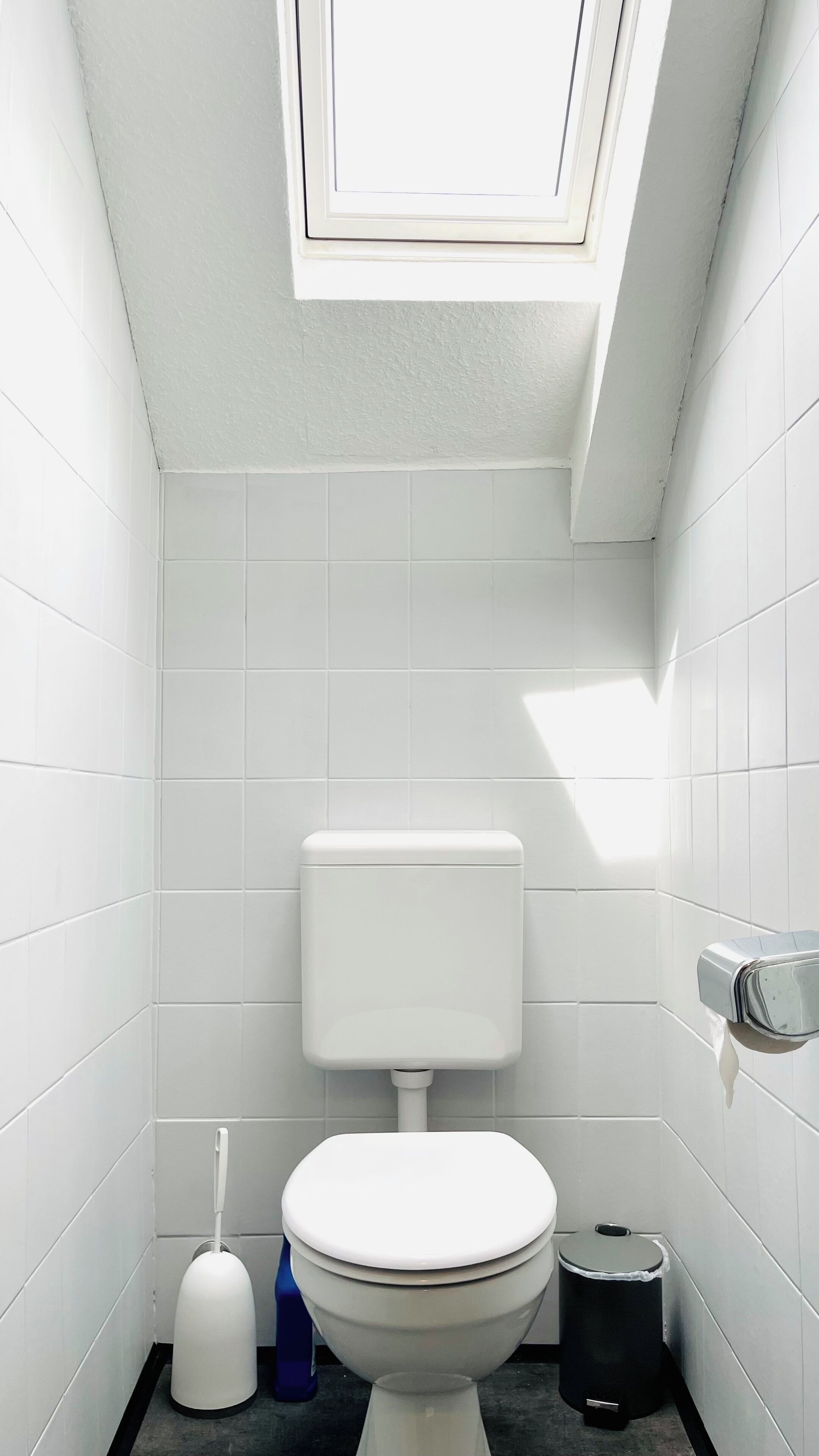 A small, white-tiled bathroom with a toilet, bidet, and trash can.