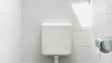 A small, white-tiled bathroom with a toilet, bidet, and trash can.