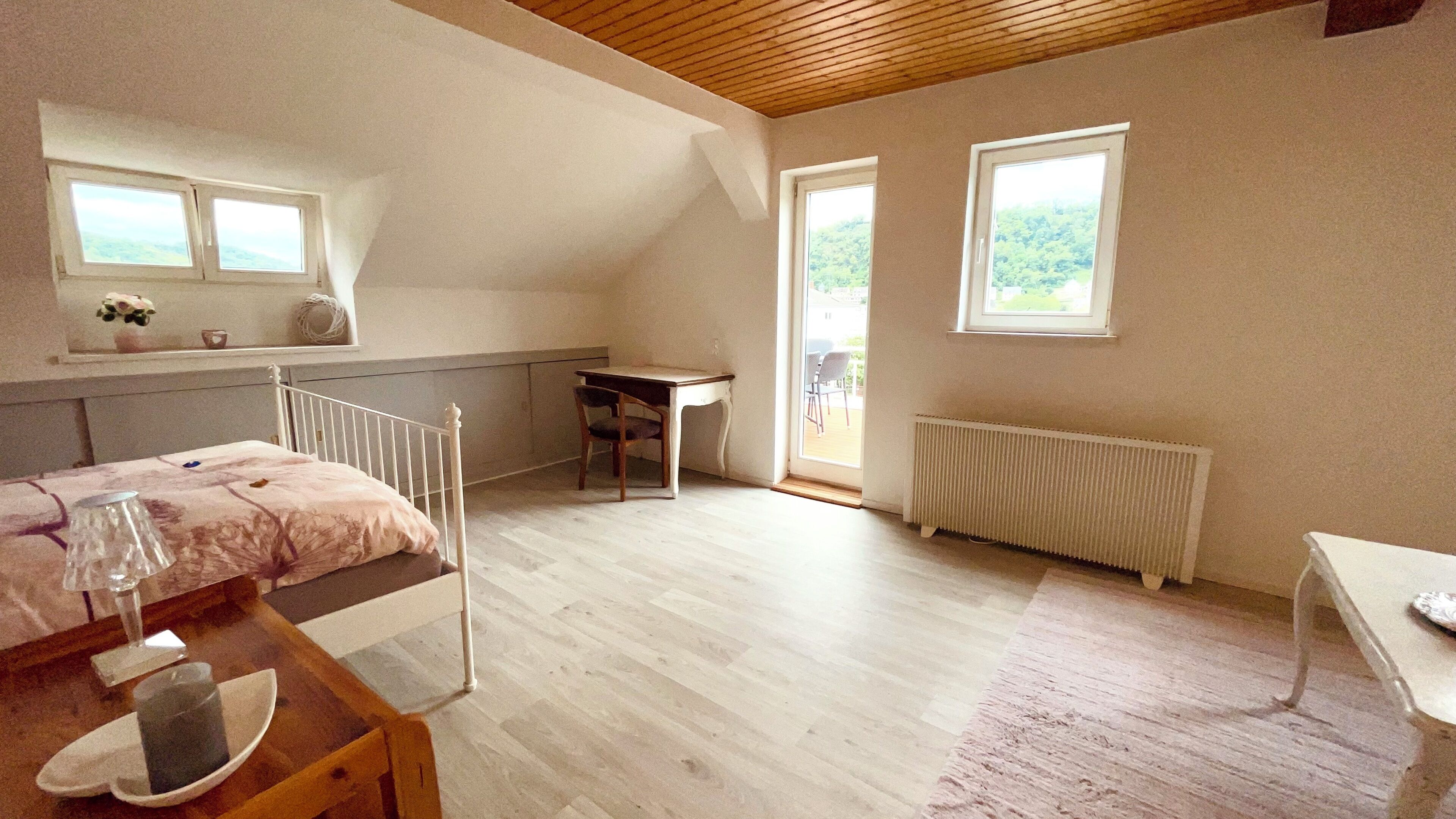 A bedroom with a bed, a table with a glass, a chair, a radiator, and two windows.. Am Rabenack (Rheinsteig)