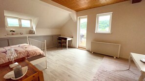 A bedroom with a bed, a table with a glass, a chair, a radiator, and two windows.