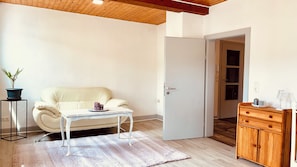 A room with a white sofa, a small white table, a wooden cabinet, and a door leading to another room.