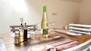 A dining table with a bottle of wine, glasses, condiments, and a placemat with a coffee cup design.