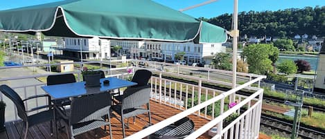 A deck with outdoor seating, a barbecue grill, and a view of a town with buildings and a river.