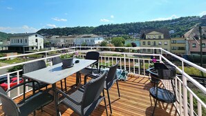 A deck with outdoor seating, overlooking a town and a river. - Am Rabenack (Rheinsteig) (Sankt Goarshausen)