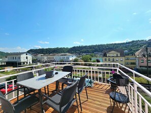 Eine Terrasse mit Sitzgelegenheiten, mit Blick auf eine Stadt und einen Fluss.