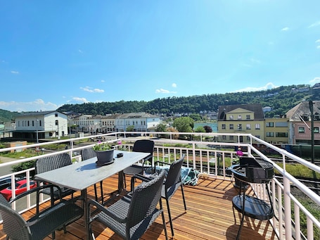 A deck with outdoor seating, overlooking a town and a river.. Am Rabenack (Rheinsteig)