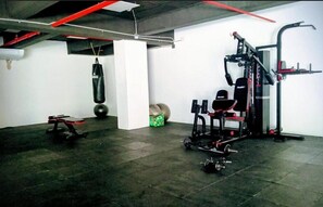 Une salle de sport Ă©quipĂ©e de matĂ©riel dâexercice, dâun sac de frappe et dâun banc de musculation.