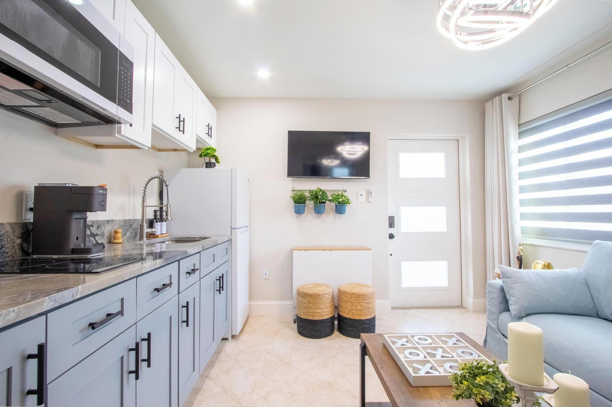 A modern kitchen with a microwave, coffee maker, and potted plants. There is a seating area with a sofa and a coffee table.. The Longwood Escape • Modern Private Guesthouse Near Orlando