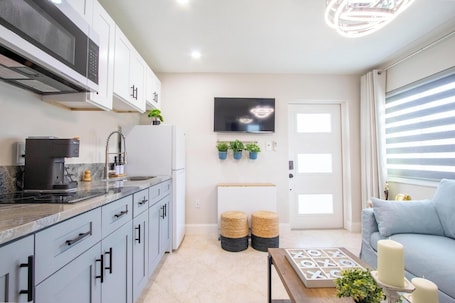 A modern kitchen with a microwave, coffee maker, and potted plants. There is a seating area with a sofa and a coffee table.. The Longwood Escape • Modern Private Guesthouse Near Orlando