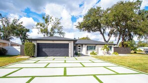 Uma casa residencial com garagem, calçada com padrão geométrico e gramado.