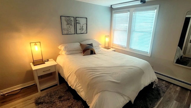 Een slaapkamer met een bed, nachtlampjes, een nachtkastje, een spiegel en twee kunstwerken aan de muur.