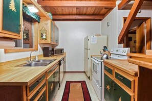A compact kitchen with wooden cabinets, a sink, a microwave, a stove, and a refrigerator. - Moose Cabin Ideally Located (Cedar Flat)