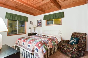 Ein Schlafzimmer mit Holzboden, einem Bett mit farbenfroher Steudecke, einem Sessel mit gemustertem Kissen und einem Nachttisch mit Lampe.