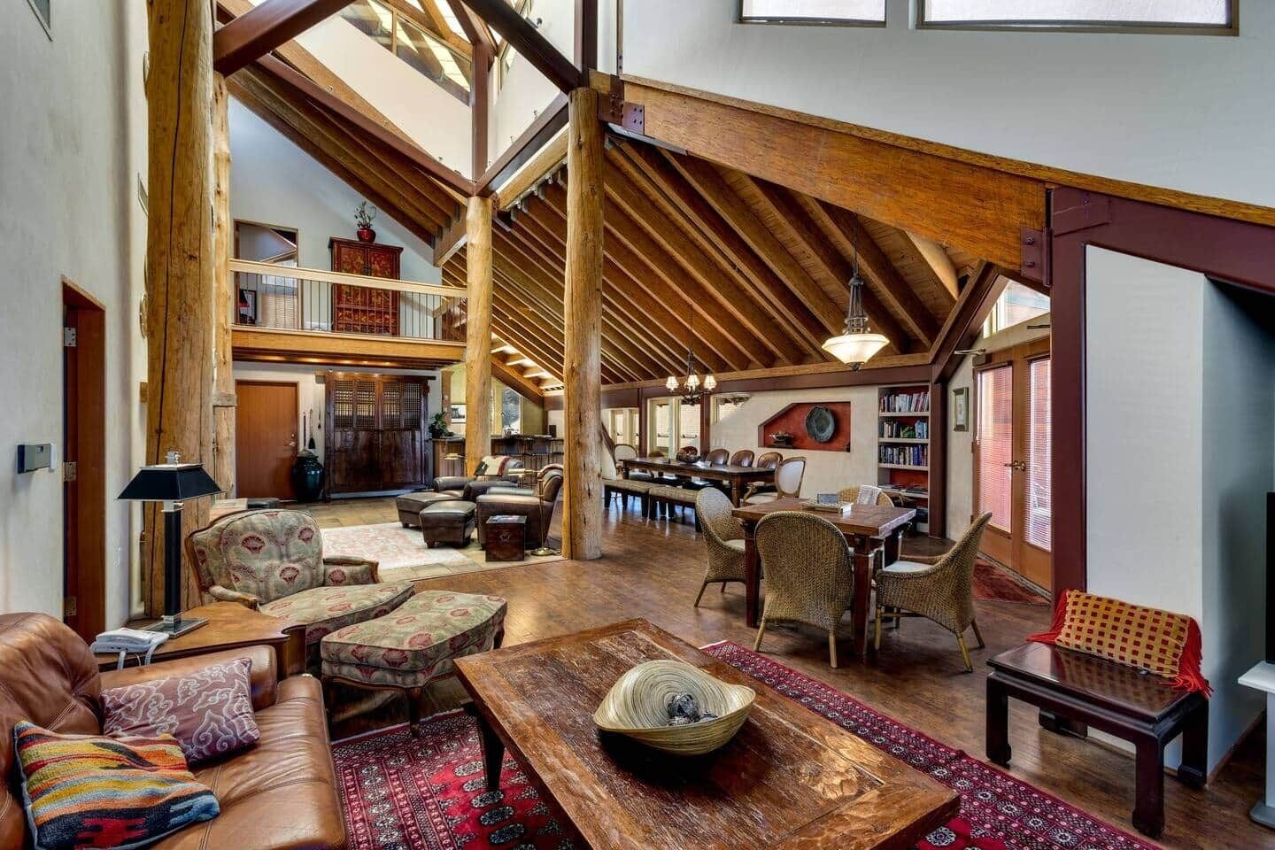 A spacious loft with high ceilings, exposed wooden beams, a dining area, and a library.