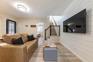 Ein Wohnzimmer mit einer Couch, einem Couchtisch, einem an der Wand montierten Fernseher und einer Treppe, die zu einer anderen Ebene führt.