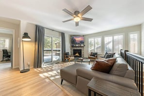 Ein geräumiges Wohnzimmer mit Kamin, Deckenventilator und großem Fenster.