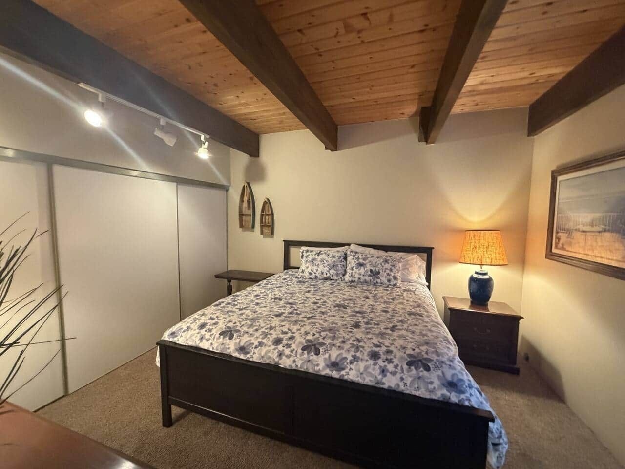 Une chambre à coucher avec un lit, une table de chevet, une lampe et un tableau encadré au mur.