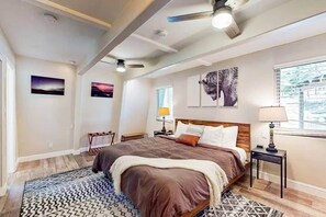 Ein Schlafzimmer mit Bett, Nachttisch, Lampe, Deckenventilator und Bildern an den Wänden.