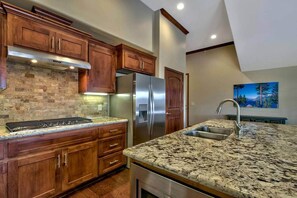 A kitchen with wooden cabinets, a stainless steel refrigerator, granite countertops, and a painting on the wall. - Ideally Located Condo - 6-min Walk to Casinos (South Lake Tahoe)
