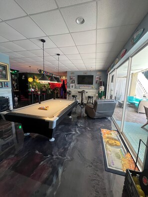 Ein Billardtisch mit Spielzeug, eine Couch, ein Fernseher und eine Treppe, die nach draußen führt.