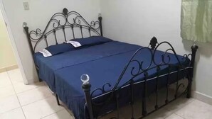Een bed met een metalen frame en een blauwe spreidekker in een kamer met betegelde vloer.