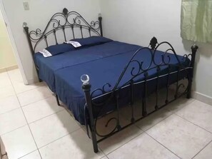A bed with a metal frame and a blue bedspread in a room with tiled flooring.
