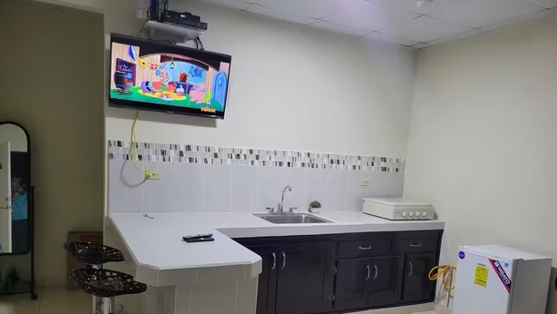 Een keuken met een televisie, een koelkast, een spoelbak en een barstoel.