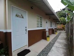 A building with a white door, a window, and a small porch area with a potted plant.