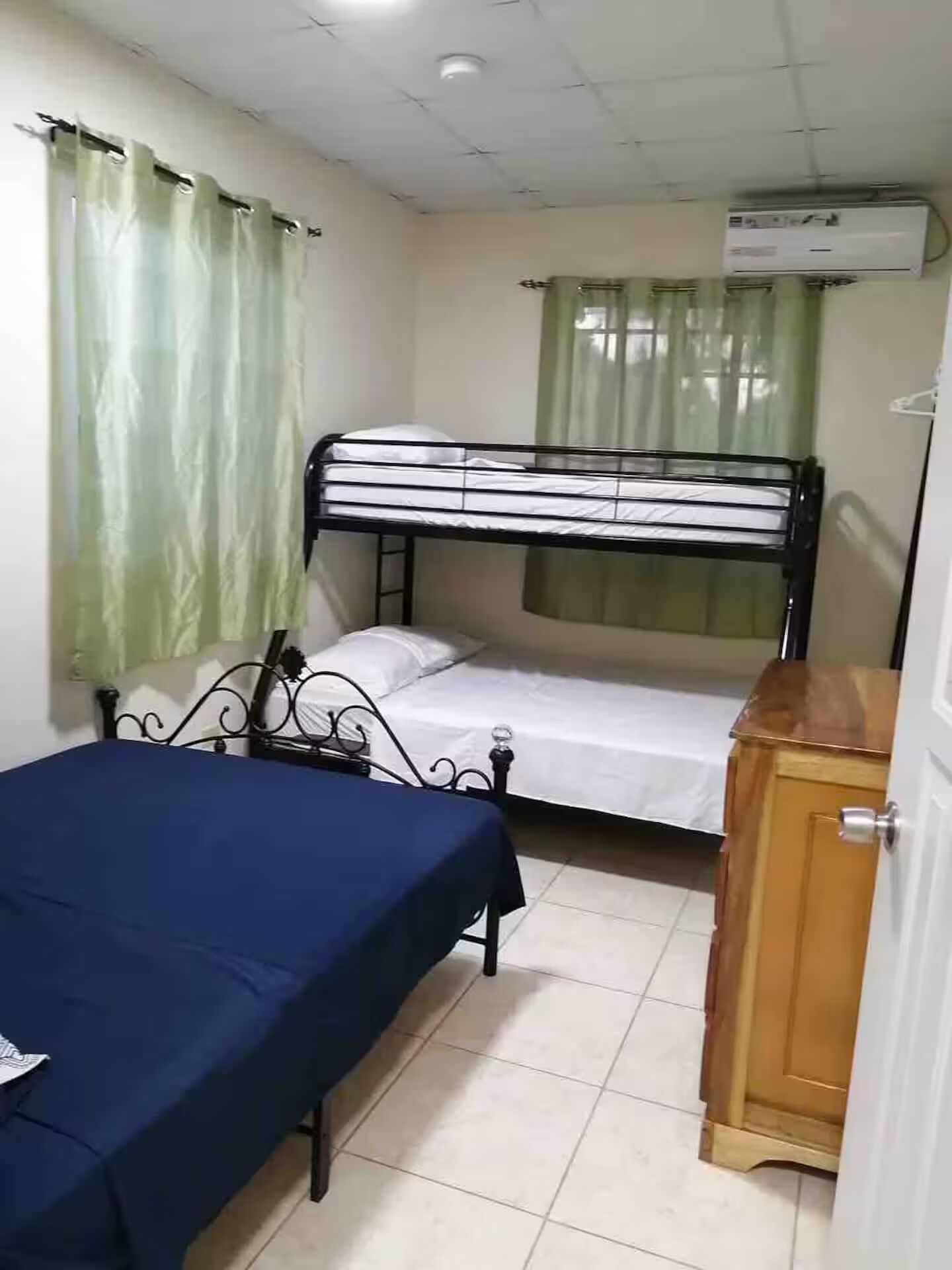 Un dormitorio con literas, una cama individual, un armario de madera y un equipo de aire acondicionado.