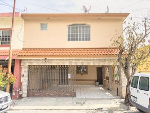 Un edificio de dos plantas con entrada protegida por un portón, techo de tejas y antena parabólica.