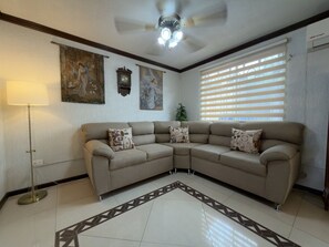 A living room with a beige sectional sofa, a floor lamp, a ceiling fan, and artwork on the walls. - Casa grande cerca del BBVA (Monterrey)