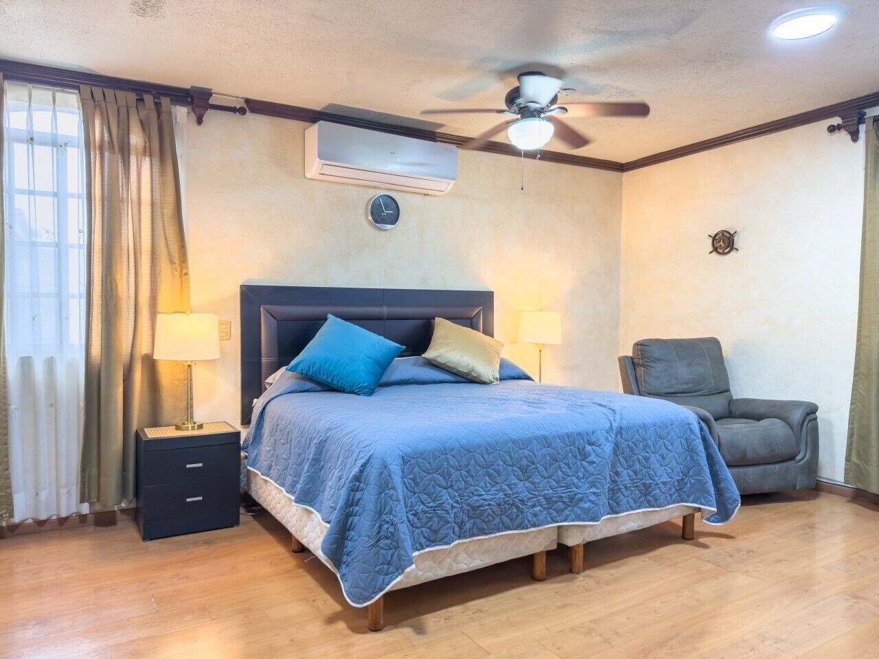 Une chambre à coucher comprenant un lit, deux tables de chevet, une chaise, un ventilateur de plafond et un appareil de climatisation.