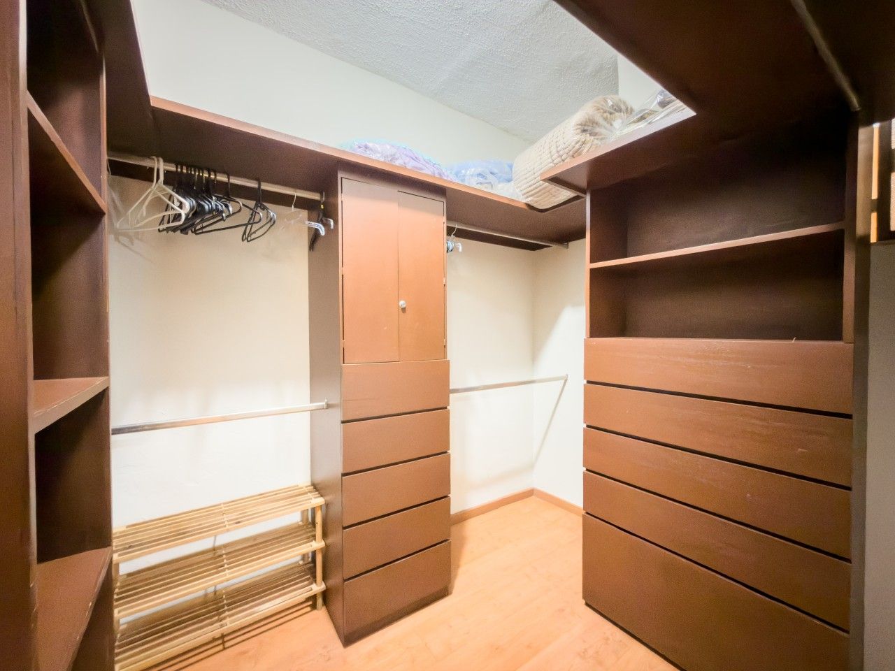 A walk-in closet with wooden shelving and a metal rack.