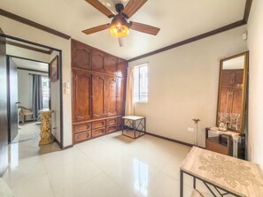 Una habitación amplia con ventilador de techo, armarios de madera, piso de baldosas y una mesita pequeña.