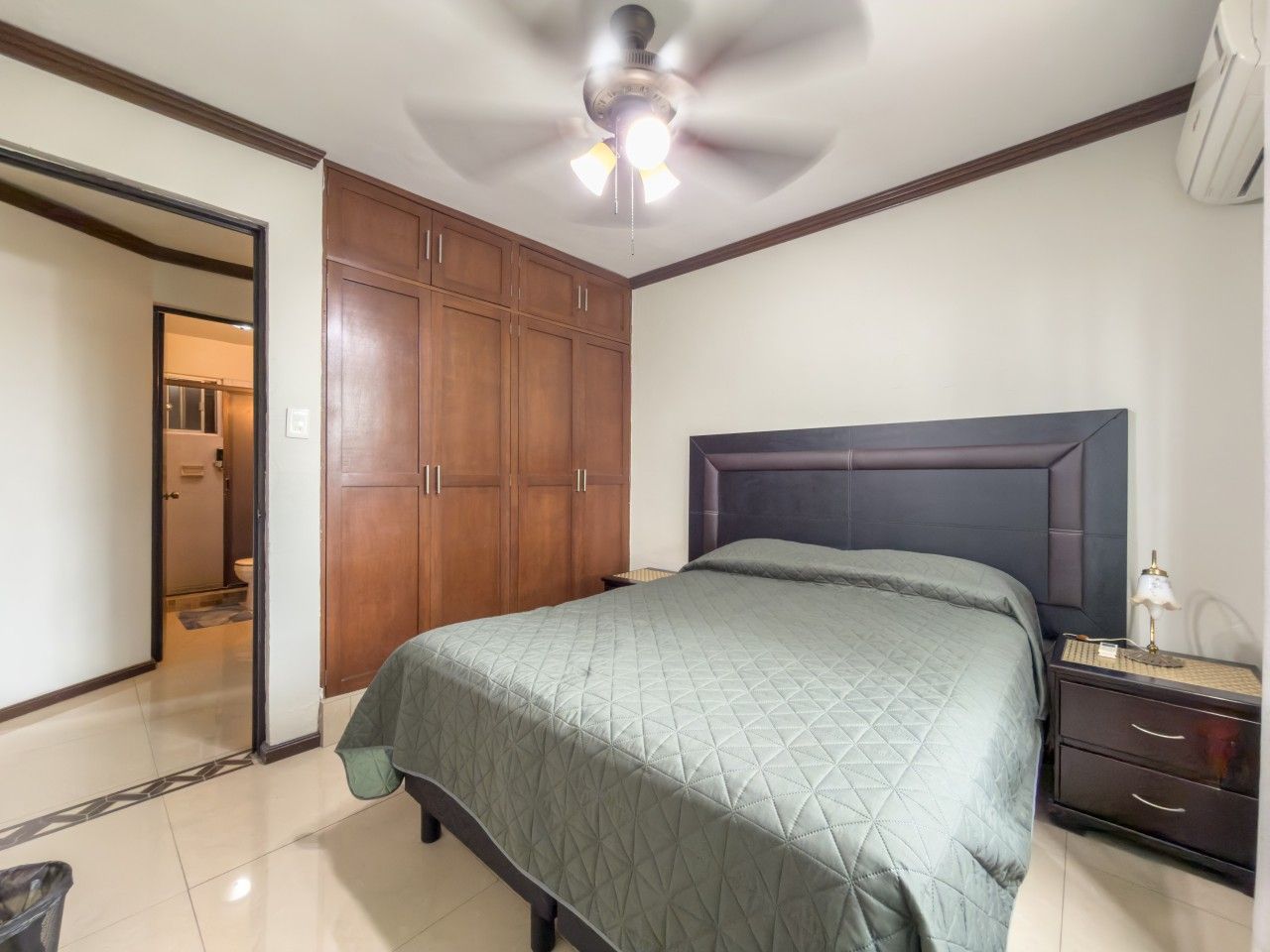 Une chambre à coucher comprenant un lit, une table de chevet, une armoire et un ventilateur de plafond.