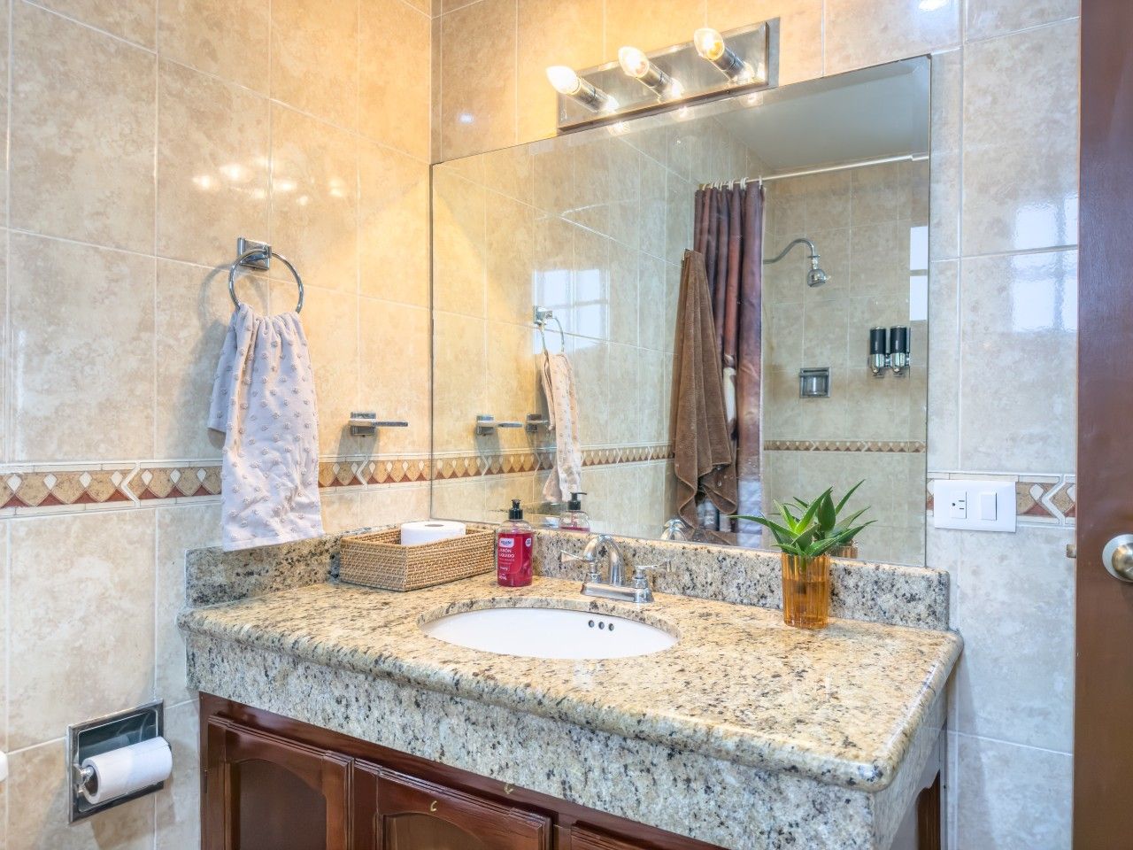 A bathroom with a granite countertop sink, a mirror, a towel rack, and a shower area.