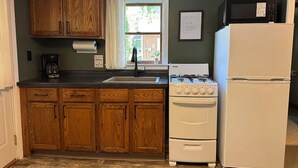 A compact kitchen with wooden cabinets, a gas stove, a microwave, and a refrigerator. - Copper Ridge at Miller's Cottages (Ontonagon)