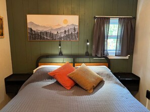 A bedroom with a bed, two nightstands, a painting, and a window with curtains.