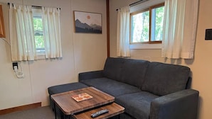 A living room with a gray sofa, a wooden coffee table, and a remote control on it. - Copper Ridge at Miller's Cottages (Ontonagon)