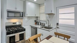 Una cocina compacta con estufa a gas, microondas, lavaplatos y gabinetes blancos.